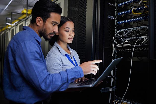 Woman with laptop and man pointing at cables in data centre