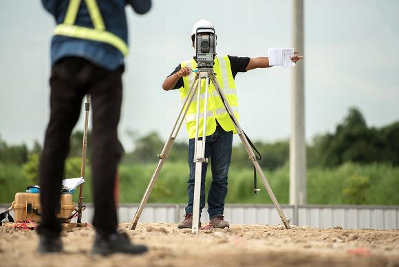 Man pointing and standing behind survey camera on construction site